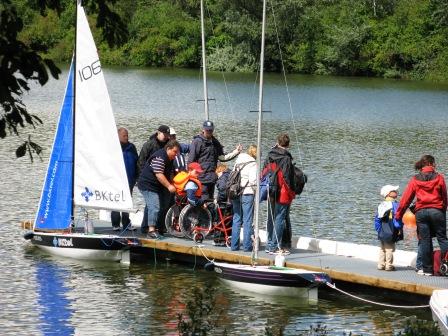 Rollifahrer steigen am Bootssteg in spezielle Minisegelboote ein. Ein Projekt der FIDS-Stiftung.